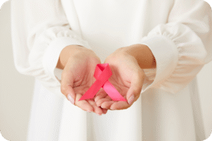 Uma mulher de blusa branca segurando uma fita rosa, símbolo do Outubro Rosa e da conscientização sobre o câncer de mama.