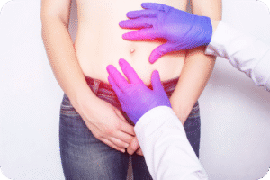 Exame físico de hérnia. Mãos de um médico, usando luvas azuis/roxas e jaleco branco, examinando o abdômen de um paciente. O umbigo e a área ao redor estão destacados com um brilho rosa/roxo, indicando o local da dor ou do abaulamento (hérnia umbilical ou epigástrica).