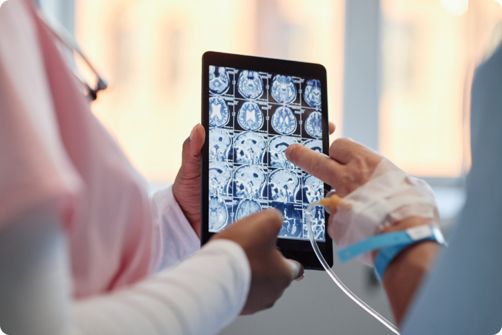 Médica e paciente analisando exames de imagem cerebral em um tablet, ilustrando a diferença entre tomografia e ressonância no diagnóstico clínico.